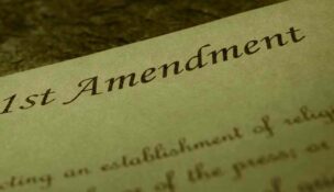 The words "1st Amendment" at the top of a piece of parchment paper with cursive text below the header to depict the U.S. Constitution