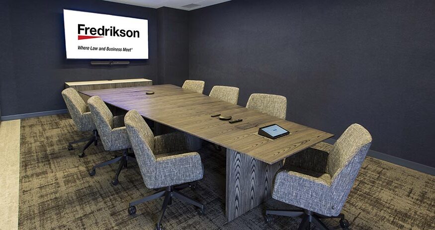 A conference room with chairs around a table and a screen to the left that has the Fredrikson logo on it
