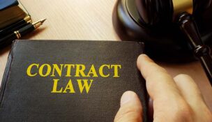 A book with a title of Contract Law resting on a desk with a person's hand near the right side of the book