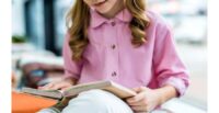Cropped view of child sitting and reading book in library
