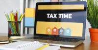 An open laptop on a desk with the words "TAX TIME" in large print across the screen