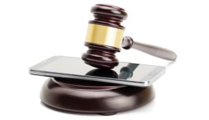 a cellphone in between a gavel and a block on a white background