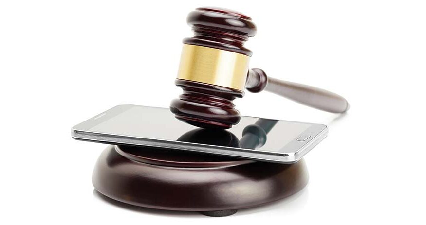 a cellphone in between a gavel and a block on a white background
