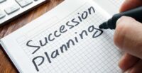 A pen shown finsihing writing "Succession Planning" on graph paper