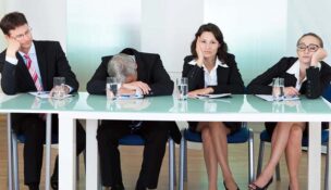 Men and women in business attire sitting behind a table and looking bored