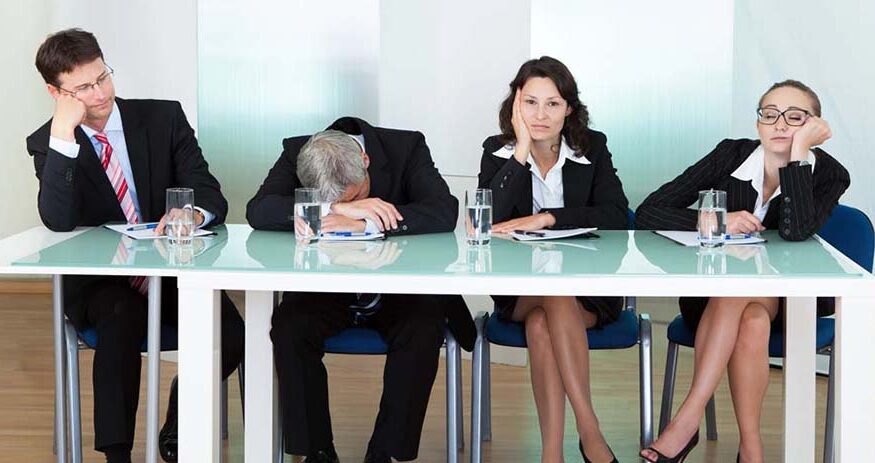 Men and women in business attire sitting behind a table and looking bored