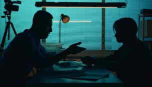 Medium silhouette shot of an perpetrator, prisoner sitting in the interrogation room in front of the detective