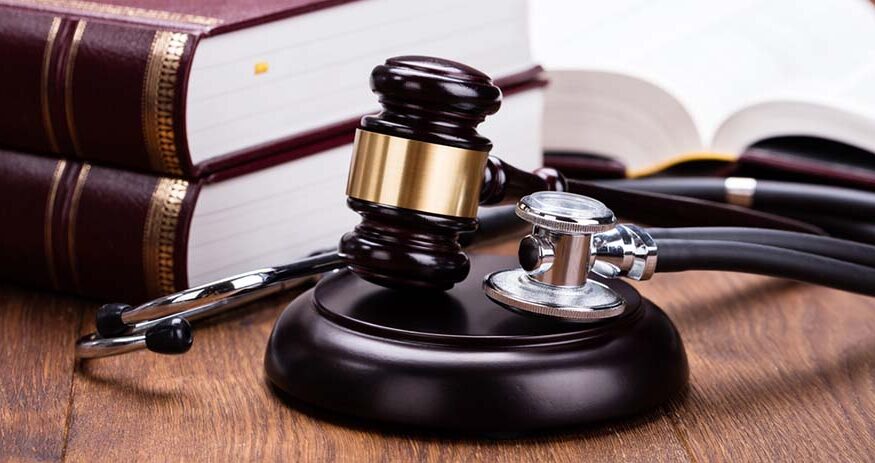 A stethoscope and gavel on a judge's block with two thick textbooks in the background