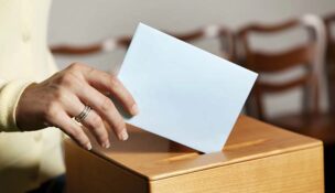 A woman's hand is shown putting a ballot into a box