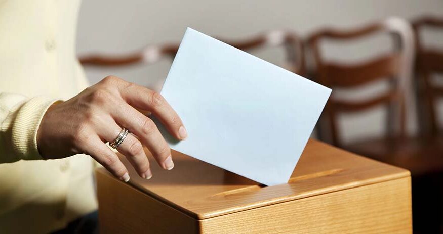 A woman's hand is shown putting a ballot into a box