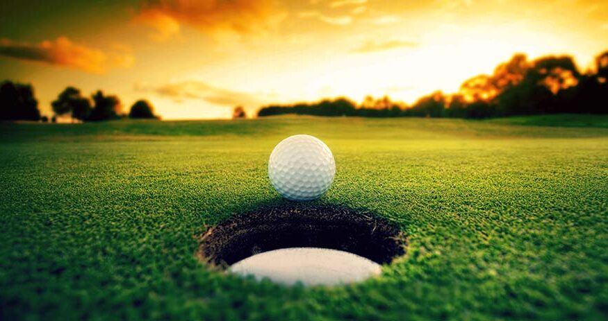 A golf ball shown just outside a hole with the sun low on the horizon